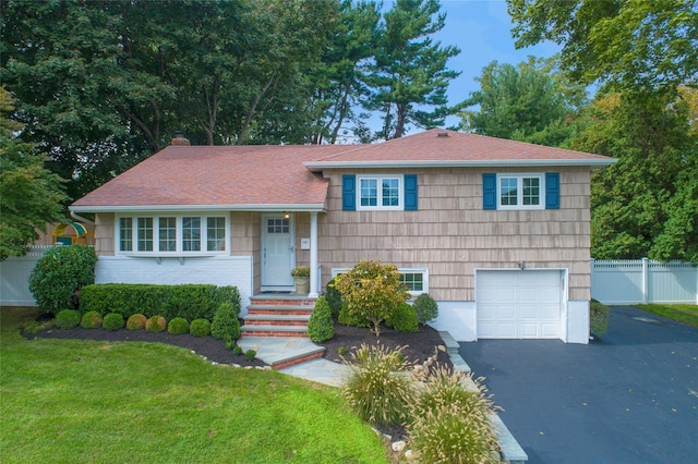 tri-level home featuring driveway, a garage, a chimney, fence, and a front lawn