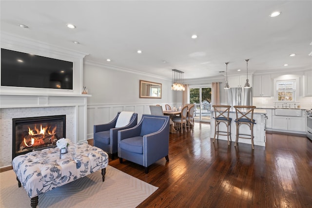 living area with recessed lighting, dark wood-style flooring, wainscoting, a glass covered fireplace, and crown molding