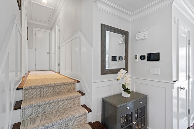 staircase with a wainscoted wall, attic access, ornamental molding, and a decorative wall