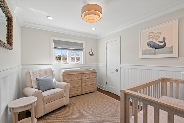 bedroom featuring a nursery area, recessed lighting, wainscoting, and crown molding