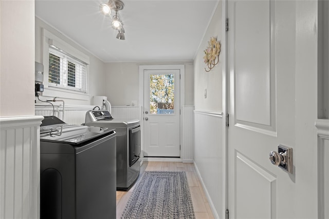 clothes washing area featuring laundry area, wood tiled floor, washer and clothes dryer, and a wainscoted wall