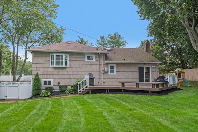 rear view of house featuring a playground, a yard, a chimney, fence, and a deck