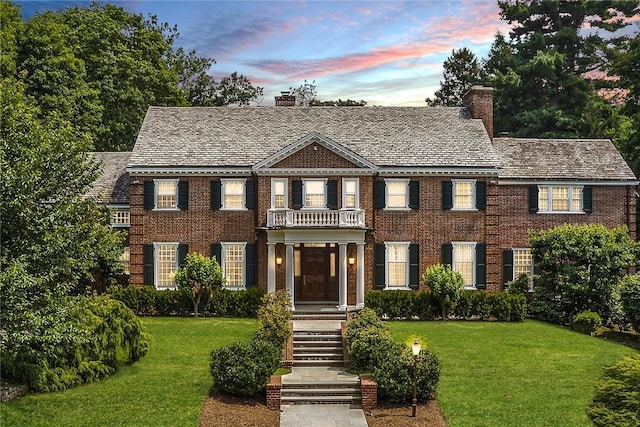 colonial home with a chimney, a front lawn, and brick siding