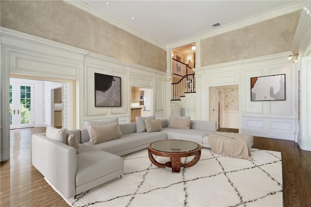 living room with crown molding, wood finished floors, a decorative wall, and stairs