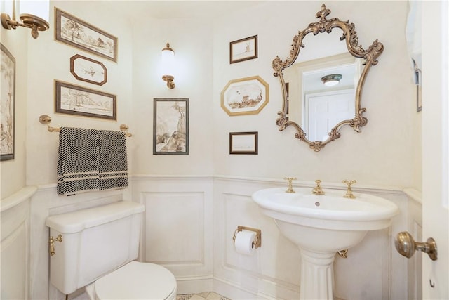 half bath featuring toilet, a decorative wall, and wainscoting