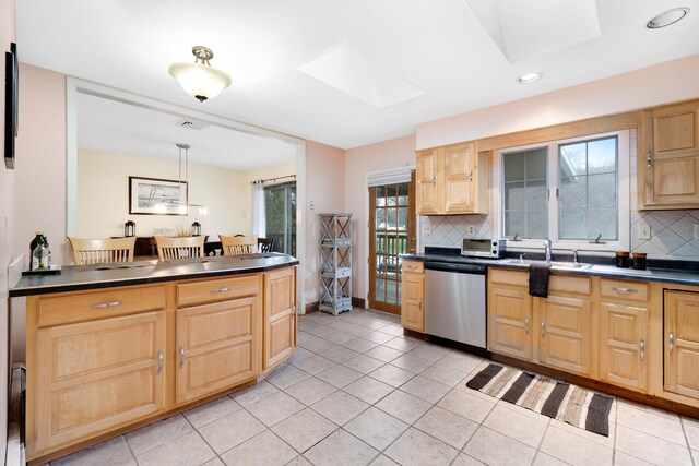 kitchen featuring stainless steel dishwasher, a skylight, a sink, dark countertops, and light brown cabinets