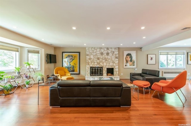 living room featuring recessed lighting, visible vents, radiator heating unit, a stone fireplace, and wood finished floors