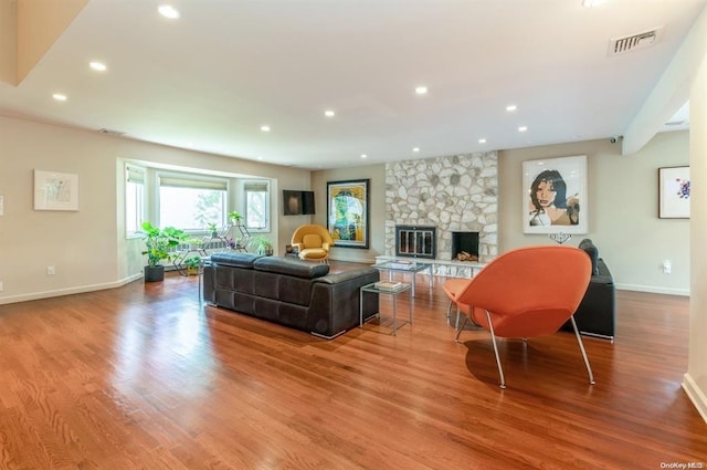 living area featuring baseboards, visible vents, wood finished floors, a stone fireplace, and recessed lighting