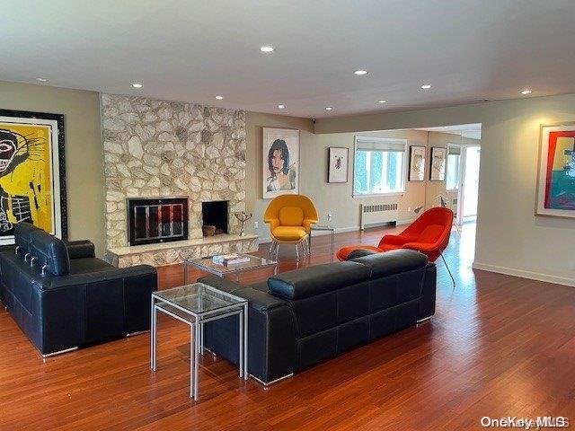 living room featuring a stone fireplace, radiator heating unit, wood finished floors, and baseboards