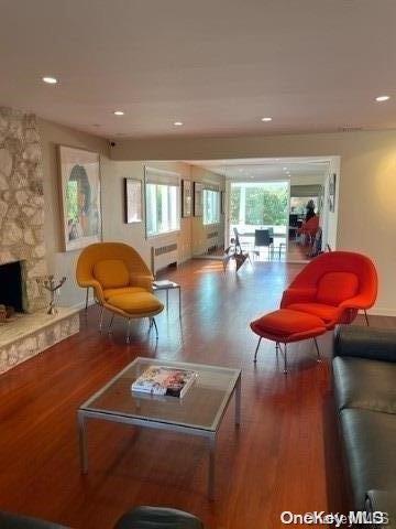 living room featuring recessed lighting, radiator, a stone fireplace, and wood finished floors