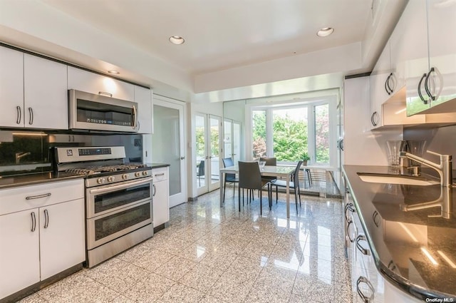 kitchen with recessed lighting, granite finish floor, a sink, appliances with stainless steel finishes, and dark countertops