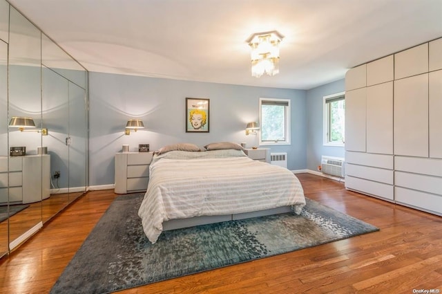 bedroom featuring radiator heating unit, baseboards, wood finished floors, and a wall mounted AC