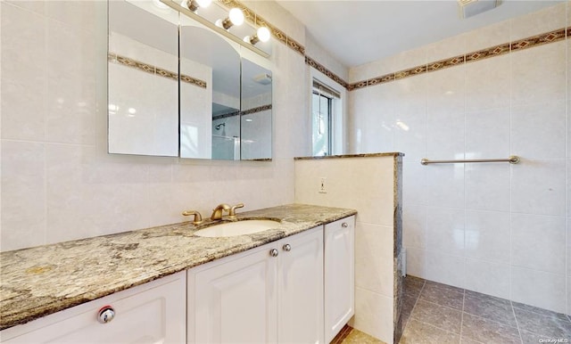 bathroom with walk in shower, tile patterned flooring, vanity, and tile walls