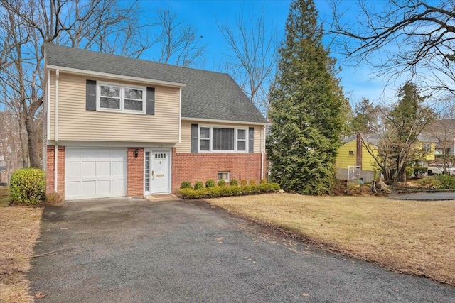 tri-level home with brick siding, a front lawn, a shingled roof, and aphalt driveway