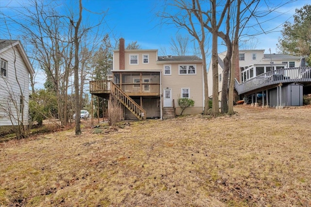 rear view of house with a lawn, a sunroom, a chimney, stairs, and a wooden deck