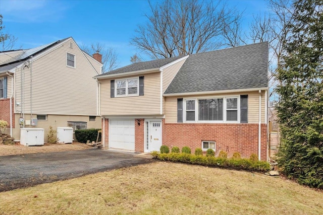 tri-level home featuring aphalt driveway, a garage, brick siding, a chimney, and a front yard