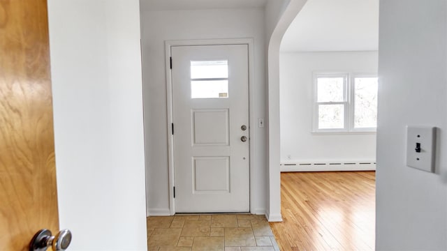 foyer entrance featuring arched walkways, baseboard heating, baseboards, and light wood-style floors