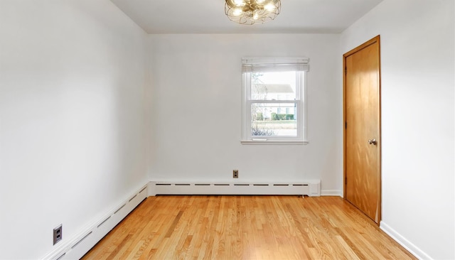 spare room featuring a baseboard heating unit, light wood finished floors, and an inviting chandelier