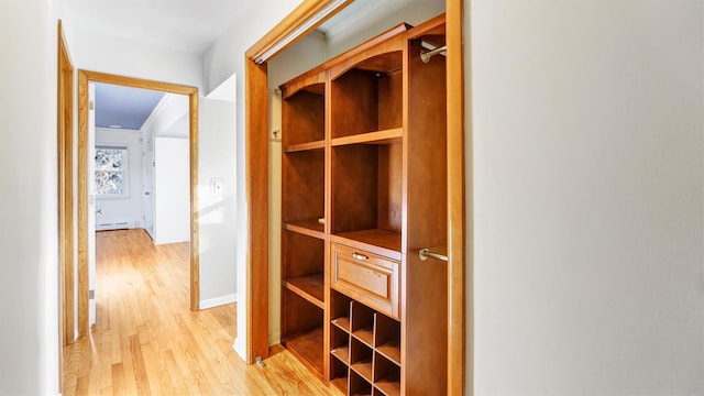 corridor featuring light wood-style floors, a baseboard radiator, and baseboards