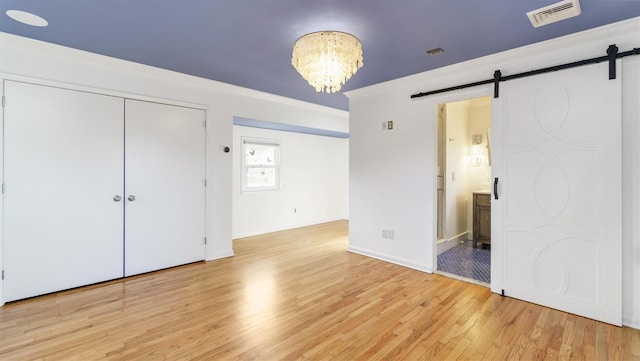 unfurnished bedroom with crown molding, a barn door, visible vents, and light wood-style floors