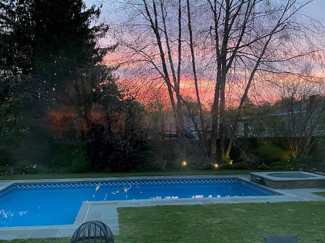 pool at dusk with an in ground hot tub, a lawn, and an outdoor pool