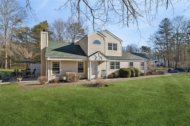 rear view of house featuring a patio area, roof with shingles, a chimney, and a yard