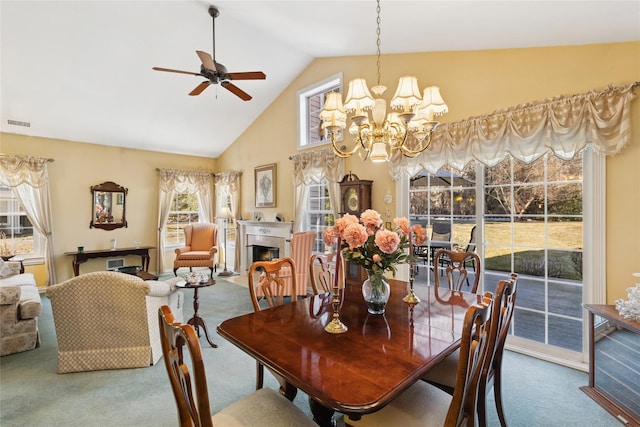 dining space featuring carpet floors, visible vents, high vaulted ceiling, a warm lit fireplace, and ceiling fan with notable chandelier