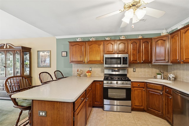 kitchen featuring stainless steel appliances, a breakfast bar, a peninsula, a sink, and light countertops