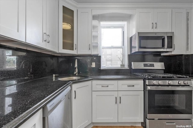 kitchen featuring dark stone counters, stainless steel appliances, a sink, and white cabinetry