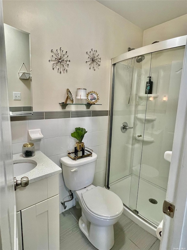 bathroom featuring a stall shower, toilet, a wainscoted wall, vanity, and tile walls