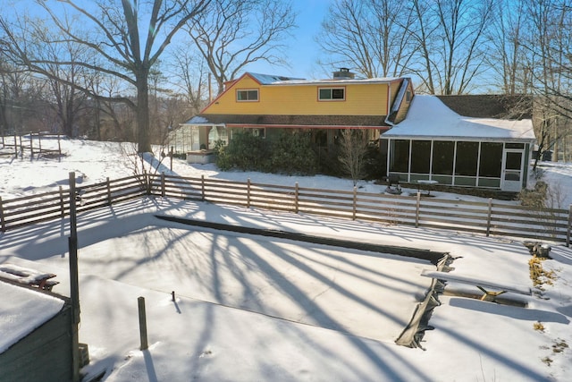 snow covered rear of property featuring a chimney, fence, and a sunroom