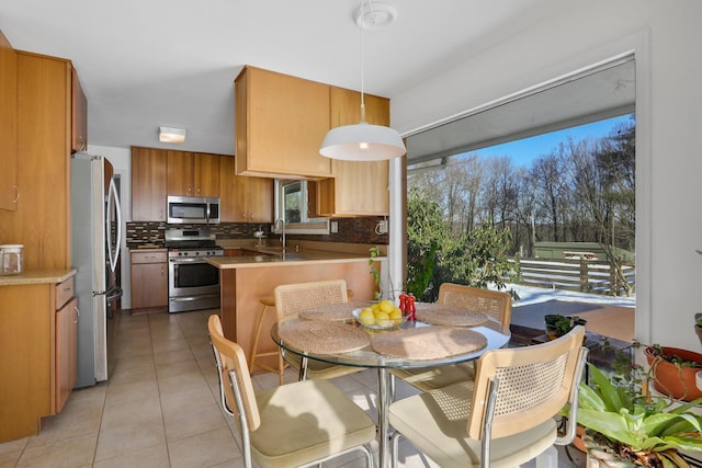 kitchen featuring light tile patterned floors, stainless steel appliances, a peninsula, tasteful backsplash, and pendant lighting