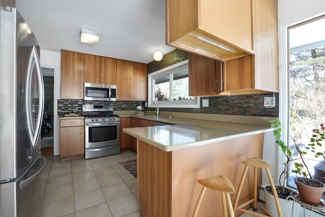 kitchen featuring light tile patterned floors, decorative backsplash, a peninsula, stainless steel appliances, and light countertops