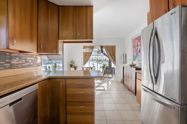 kitchen featuring appliances with stainless steel finishes, brown cabinets, a peninsula, light countertops, and light tile patterned flooring