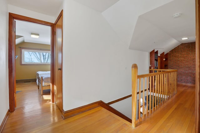 hall with lofted ceiling, brick wall, light wood-type flooring, and an upstairs landing