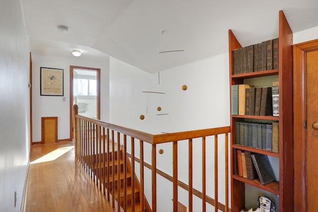 hallway featuring lofted ceiling, light wood-type flooring, an upstairs landing, and baseboards