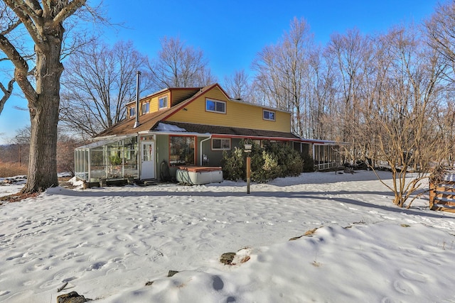 snow covered rear of property with a hot tub