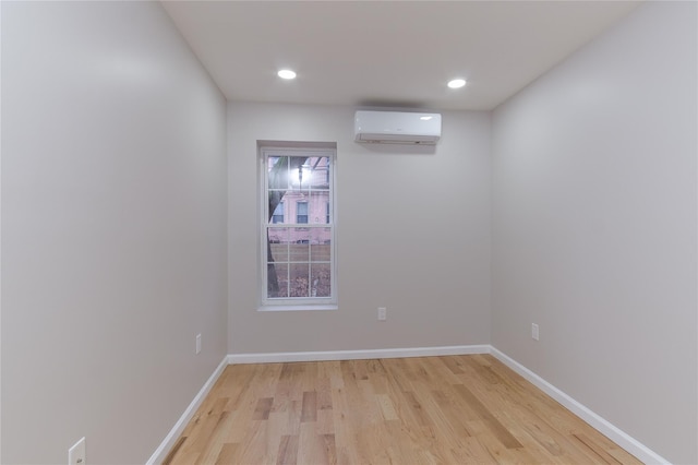 empty room with a wall unit AC, light wood finished floors, baseboards, and recessed lighting