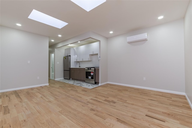 unfurnished living room with light wood-type flooring, an AC wall unit, baseboards, and recessed lighting