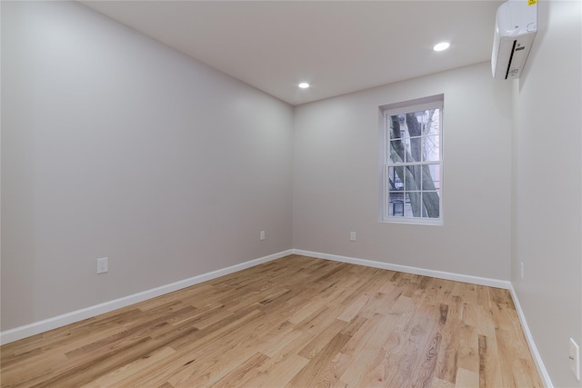 unfurnished room featuring an AC wall unit, light wood finished floors, recessed lighting, and baseboards