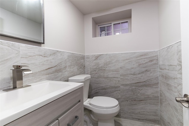 half bath with toilet, wainscoting, tile walls, and vanity