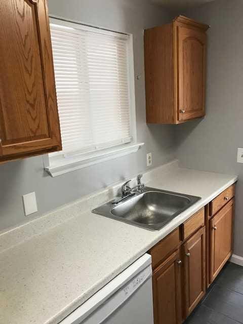 kitchen featuring dishwasher, light countertops, a sink, and brown cabinets