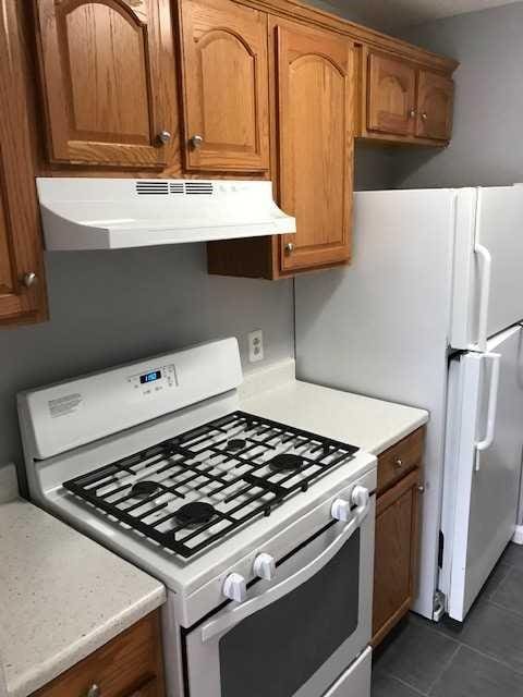 kitchen featuring white gas stove, under cabinet range hood, dark tile patterned floors, light countertops, and brown cabinets