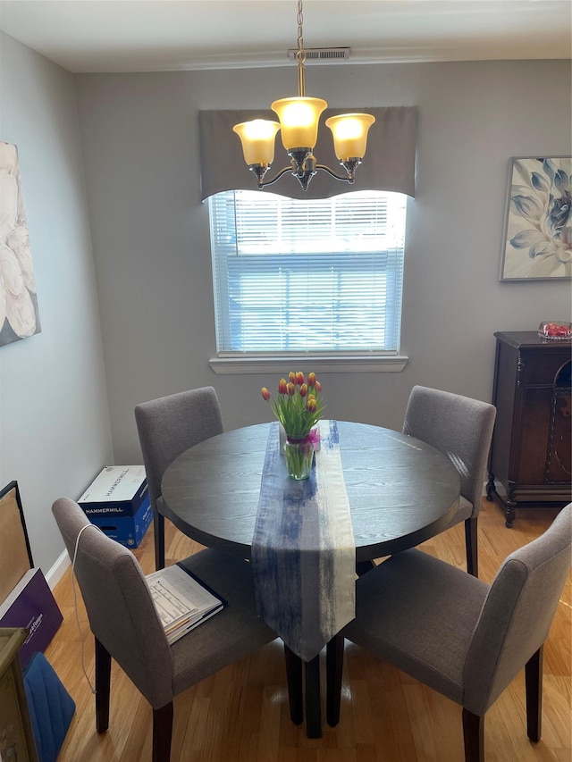 dining space with wood finished floors, visible vents, and a notable chandelier