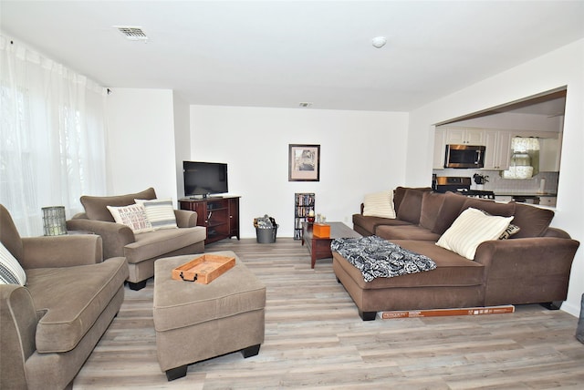 living area with light wood-style flooring, visible vents, and a healthy amount of sunlight