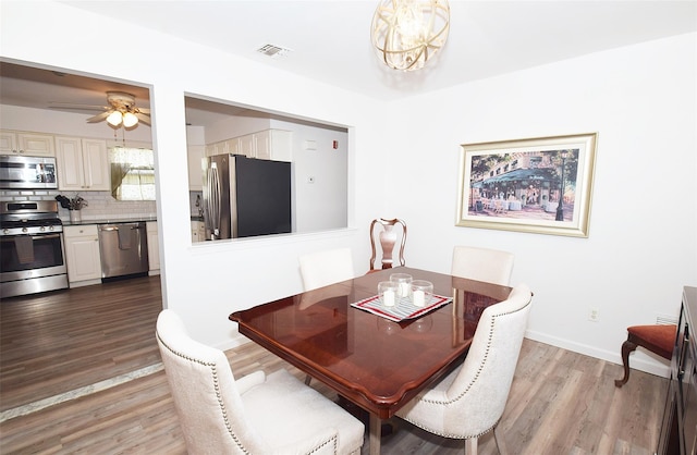 dining space featuring ceiling fan with notable chandelier, wood finished floors, visible vents, and baseboards