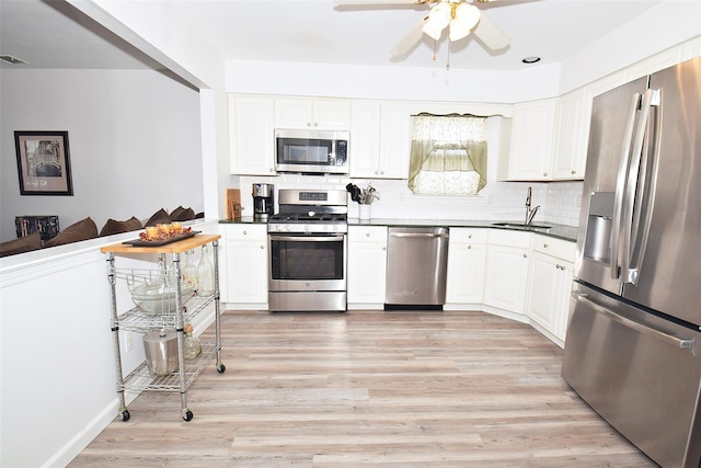 kitchen with light wood finished floors, stainless steel appliances, dark countertops, tasteful backsplash, and a sink