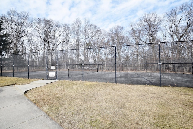 view of tennis court with a gate, fence, and a lawn