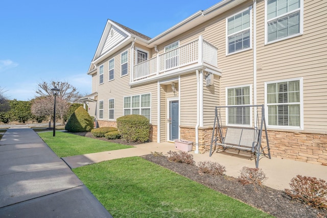 townhome / multi-family property featuring a balcony, stone siding, and a front lawn