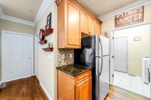 kitchen featuring tasteful backsplash, dark stone countertops, wood finished floors, freestanding refrigerator, and crown molding